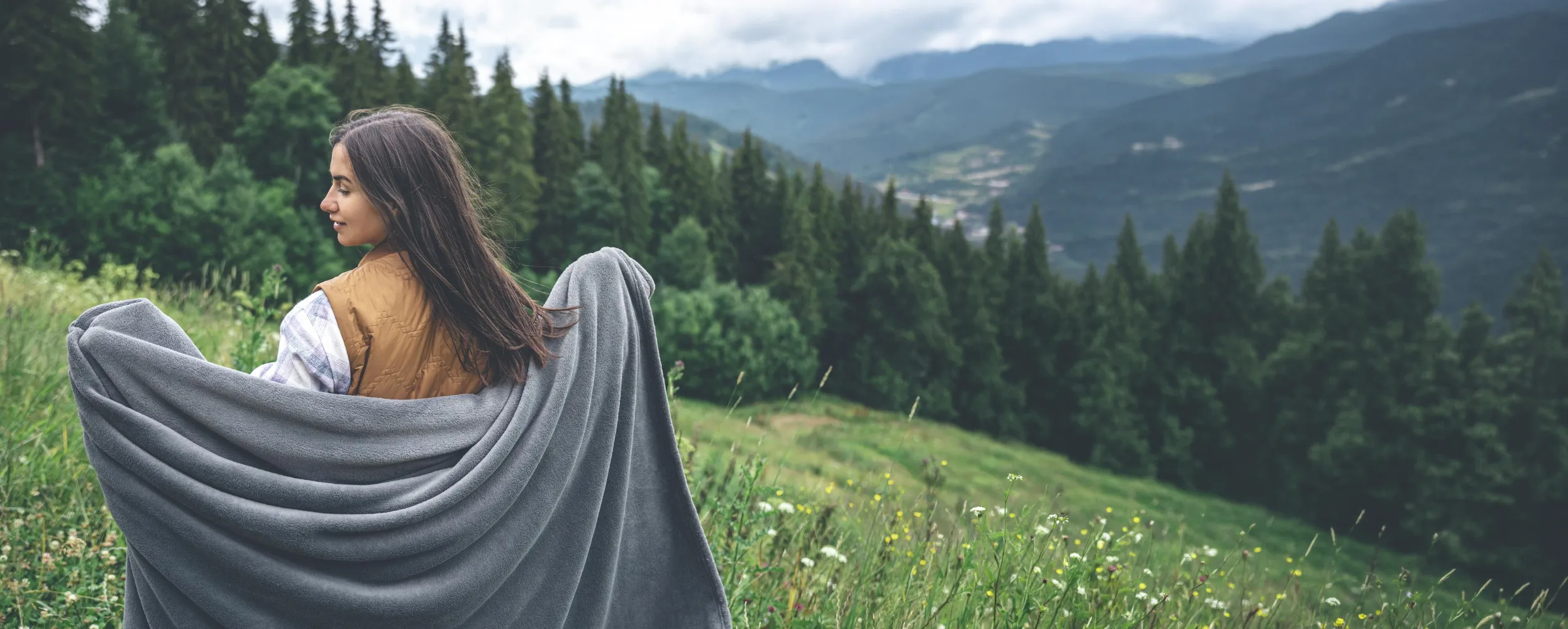 A woman wrapped in a grey fleece blanket on a mountain meadow